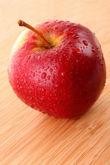 Red apple on wooden surface with water drops