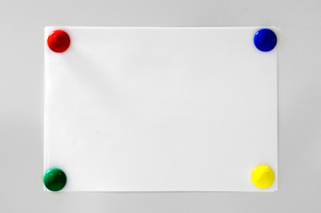 White paper hanging on grey background with four magnets