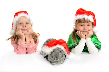 Two girls with a rabbit in red caps of Santy over white