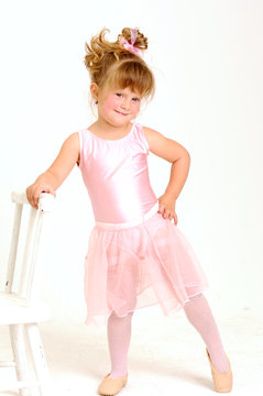 Little smiley girl wearing a pink ballet outfit is dancing