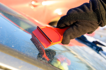 Cleaning windscreen from ice and snow with red scraper - obrazy, fototapety, plakaty