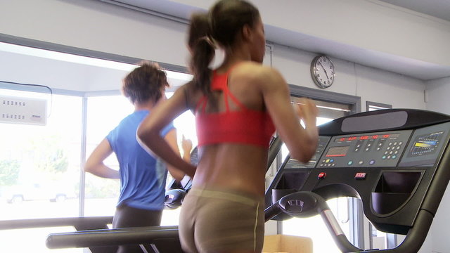 Two young women friends running on treadmill at gym