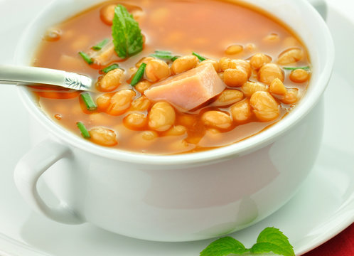 bean soup with ham and tomatoes in a white soup cup