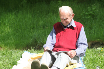 Rüstiger Rentner beim Lesen eines Buches in grüner Natur