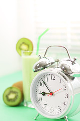 Kiwi juice in a glass and alarm clock on a light background