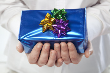 Female caucasian hands holding out a blue gift.