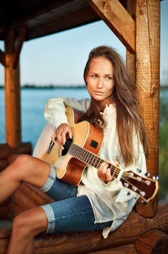 Young woman playing guitar in summerhouse on sunset
