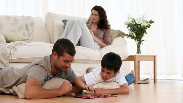 Father and son playing checkers lying on the floor