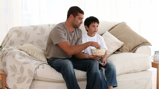 Happy man watching television with his son sitting on the sofa