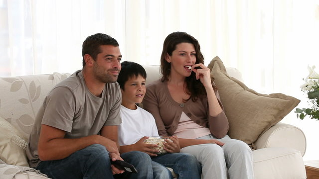 Happy family watching a movie and eating pop corn on the sofa