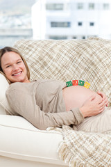 Glad woman with baby letters on her belly lying on the sofa