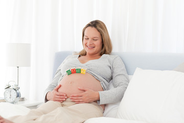 Woman looking at baby letters on her belly on her bed