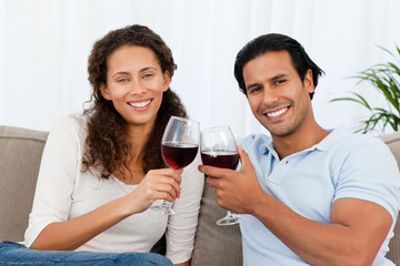 Portrait of a couple clinking glasses of red wine on the sofa