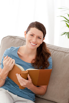 Happy woman holding a photo album sitting on her sofa