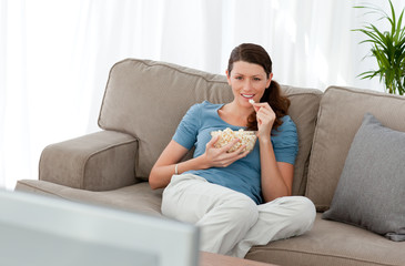 Obraz premium Attractive woman watching television and eating pop corn on the