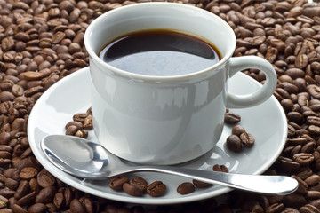 Coffee beans in white cup on saucer with spoon