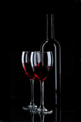Bottle and glass of red wine on black background