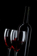 Bottle and glass of red wine on black background