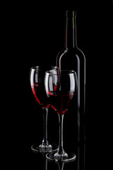 Bottle and glass of red wine on black background
