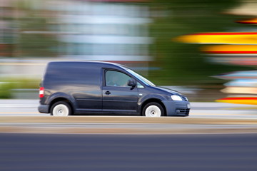 Obraz na płótnie Canvas Speedy ciemny minivan dzieje na drodze, panoramowanie i rozmycie