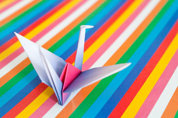 An origami bird on a colorful stripes background.