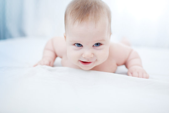 Happy smiling infant baby girl on white sheet
