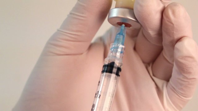 Closeup of syringe drawing medicine from a bottle.