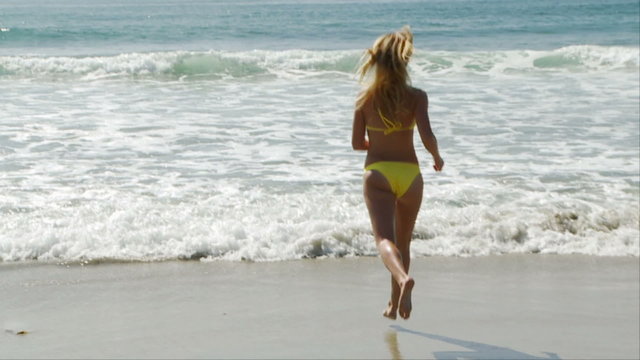 Woman in yellow bikini running into the ocean