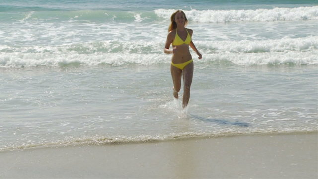 Woman in yellow bikini running out of the water at the ocean