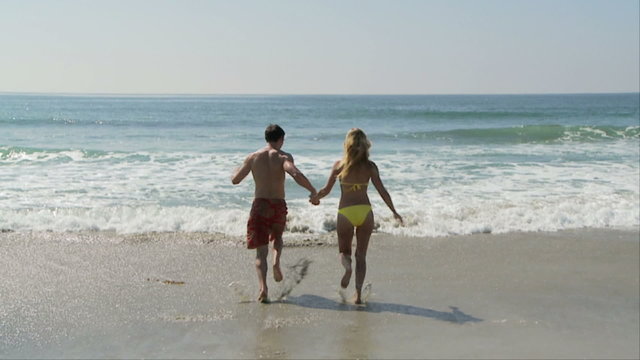 Young couple running into the ocean waves at the beach