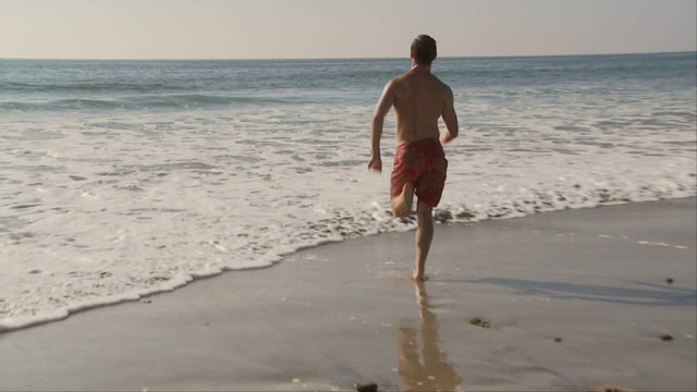 Young man running into ocean waves at beach