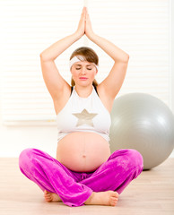 Beautiful pregnant woman doing yoga on floor at living room.