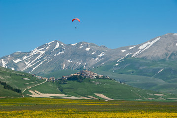 Mountain village and meadow with paraglider - obrazy, fototapety, plakaty