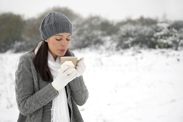 Woman holding hot drink & tissue on snowy day