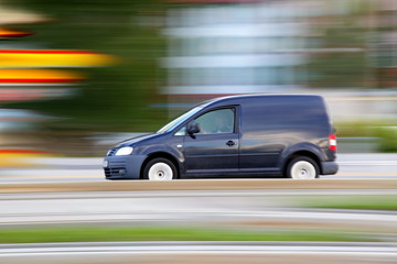 Fototapeta na wymiar Speedy dark minivan is going on road, panning and blur