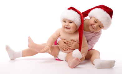 Two children wearing red Christmas caps and smile