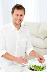 Joyful man serving salad standing at a table in the living room