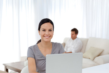 Cute woman working on the laptop while her husband relaxing