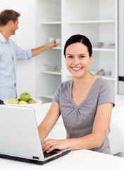 Happy woman working on the laptop in the kitchen with her boyfri