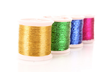 Pile of coloured bobbins of lurex thread isolated on white