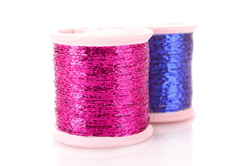 Pile of coloured bobbins of lurex thread isolated on white