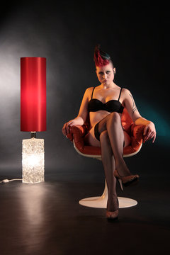 Eine Frau in Dessous im Sessel vor einer Stehlampe halbnackt im Sessel sitzend