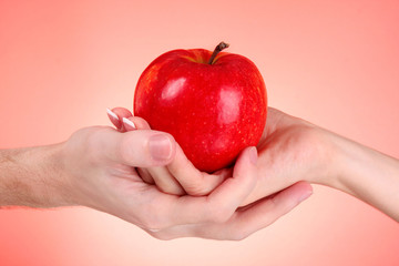 Apple between man and woman hand on red background