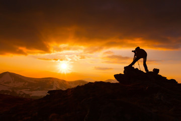 silhouette of a photographer who shoots a sunset in the mountain