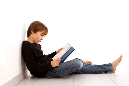 Junge liest am Boden sitzend, konzentriert ein Buch