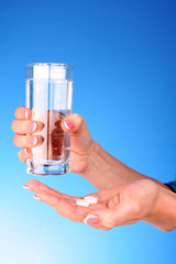 Tablets and glass of water in the woman hands on blue background