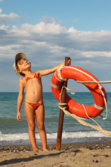 beautiful little girl in bathing suit and cap standing on beach.
