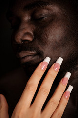 Caucasian girl with long manicure touch the face of a black man