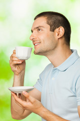 Portrait of young happy smiling man drinking coffee, outdoors