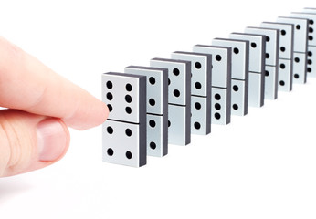 Hand ready to push domino pieces to cause chain reaction